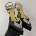 Black high-heeled shoes with heart-shaped embellishments on a light gray background