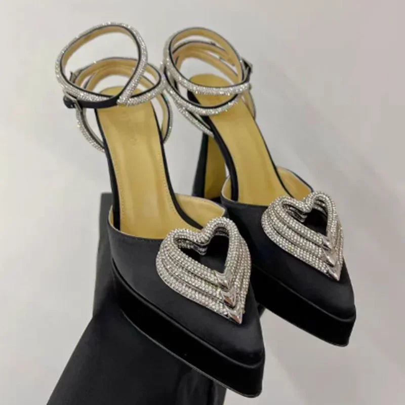 Black high-heeled shoes with heart-shaped embellishments on a light gray background