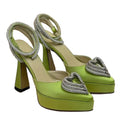 Green high-heeled shoes with decorative heart details on a neutral background