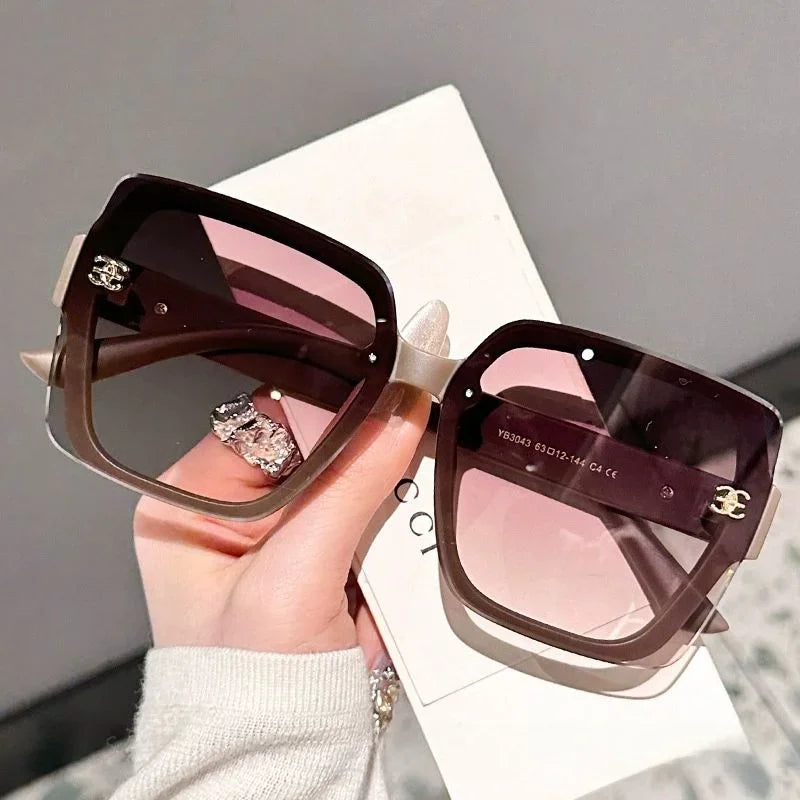 Sunglasses with a brand logo held by a hand on a neutral background