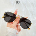 Black sunglasses with gold frame held by a hand against a light background