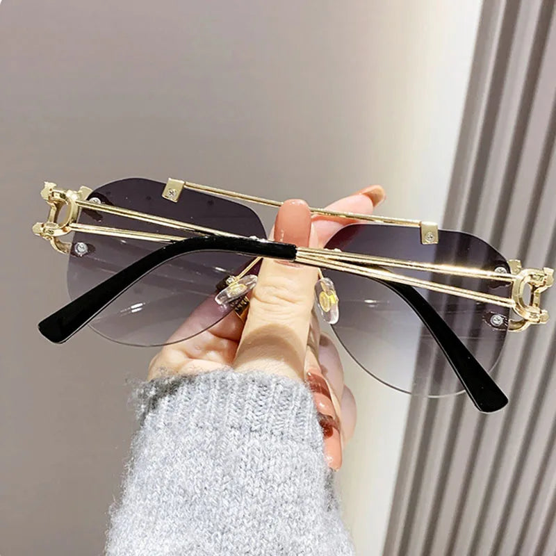 Gold-framed sunglasses with black lenses held by a person wearing a gray sweater.