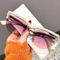 Sunglasses with pink gradient lenses held by a hand wearing an orange sweater.