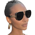 Woman wearing gold-framed sunglasses with a plain background