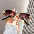 Gold-framed sunglasses with gradient lenses held by a hand against a neutral background