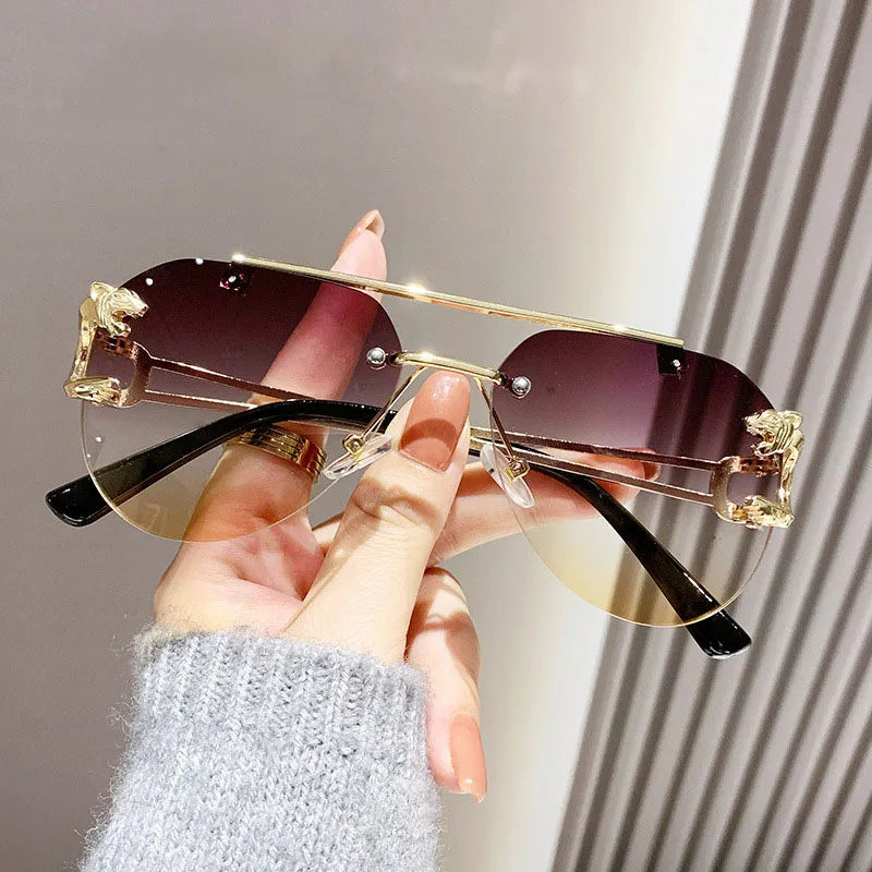 Gold-framed sunglasses with gradient lenses held by a hand against a neutral background