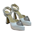 White high-heeled shoes with silver heart-shaped embellishments on a light background