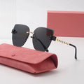 Black sunglasses with gold chain detail on a pink case against a light gray background