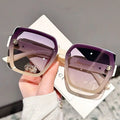 Sunglasses with purple lenses and gold frames held by a hand on a blurred background