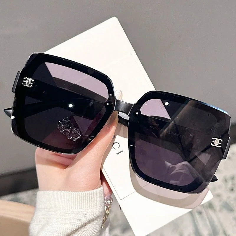 Black sunglasses with brand logo held by a hand on a neutral background