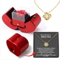 Red jewelry box with a red rose, gold necklace with heart pendant, and black card on a white background.