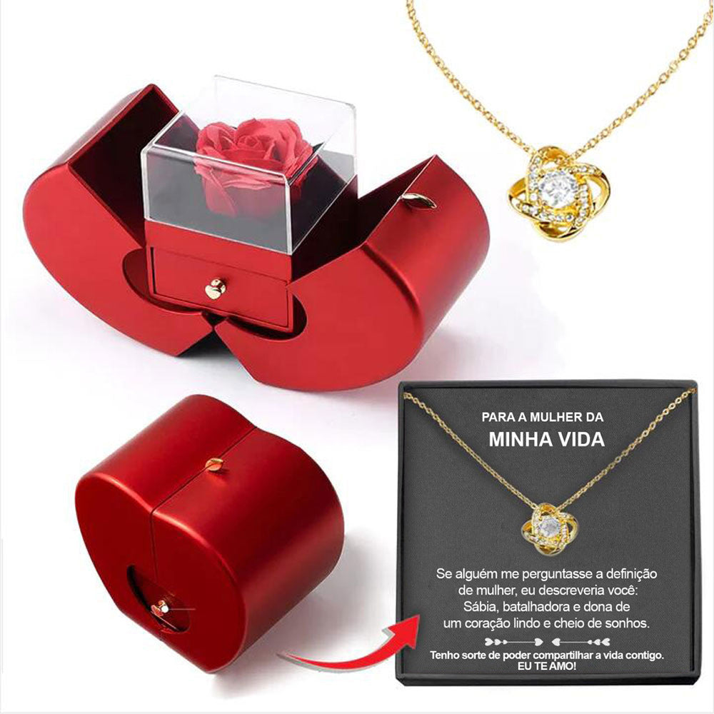 Red jewelry box with a red rose, gold necklace with heart pendant, and black card on a white background.