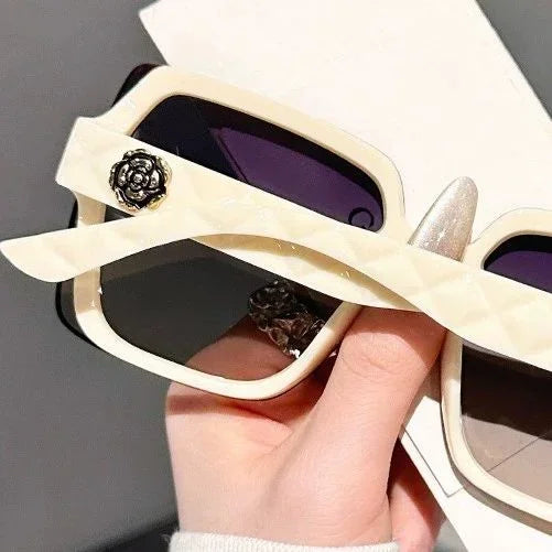 Beige sunglasses with decorative elements held by a hand against a gray background