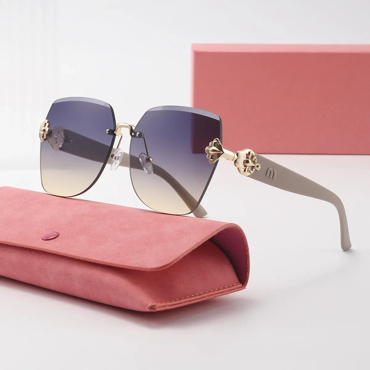 Sunglasses with gold accents on a pink case with a pink box in the background