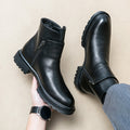 Black leather boots with zippers held by a hand on a beige background