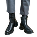 Black leather boots worn with gray pants on a white background