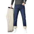 Person holding a folded beige jacket next to blue jeans on a white background