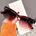 Sunglasses with gradient lenses held by a hand wearing an orange sleeve.