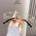 Hand holding a pair of transparent eyeglasses with gold and black frames against a neutral background.