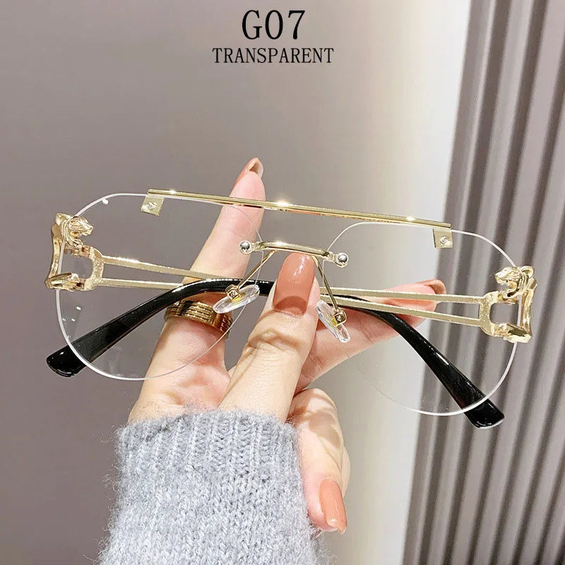 Hand holding a pair of transparent eyeglasses with gold and black frames against a neutral background.