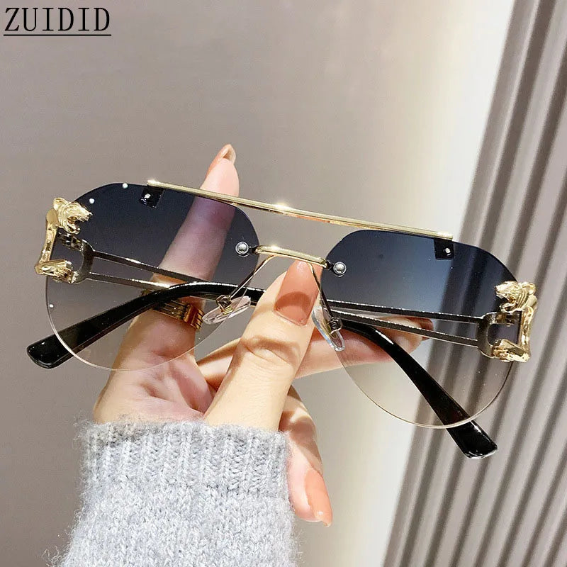Gold and black rimless sunglasses held by a hand with a neutral background