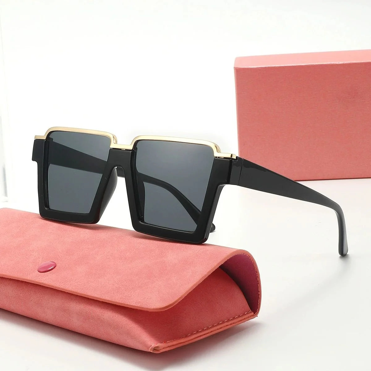 Black sunglasses with gold accents on a pink case with a matching box in the background.
