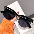Black sunglasses held by a hand with orange sleeve on a blurred background