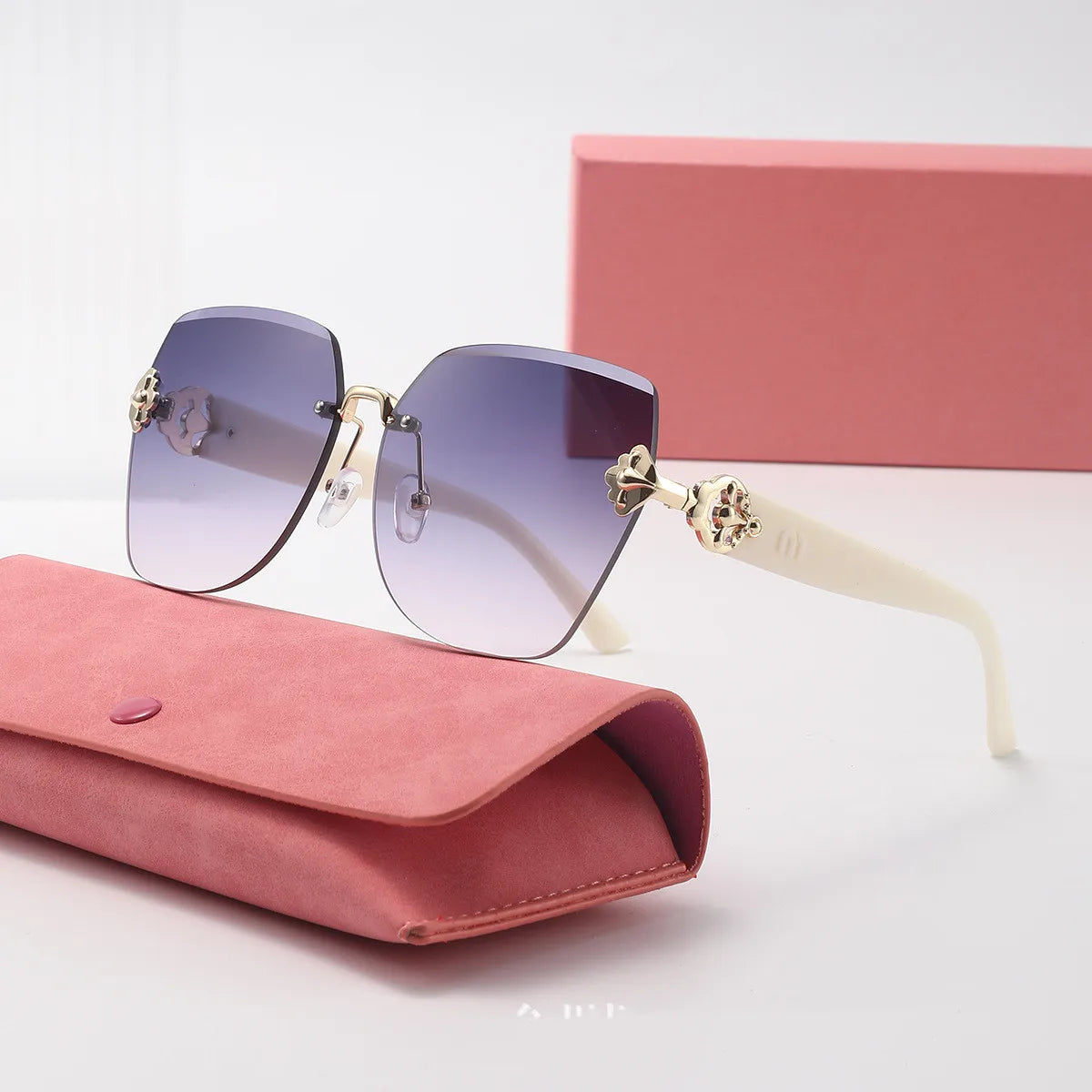 Sunglasses with gradient lenses and gold accents on a pink case with a matching box in the background.