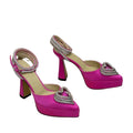 Pink high-heeled shoes with decorative heart embellishments on a pink platform box.