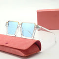 Sunglasses with blue lenses and gold frames on a pink case with a pink box in the background.