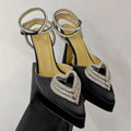 Black high-heeled shoes with heart-shaped embellishments on a light gray background