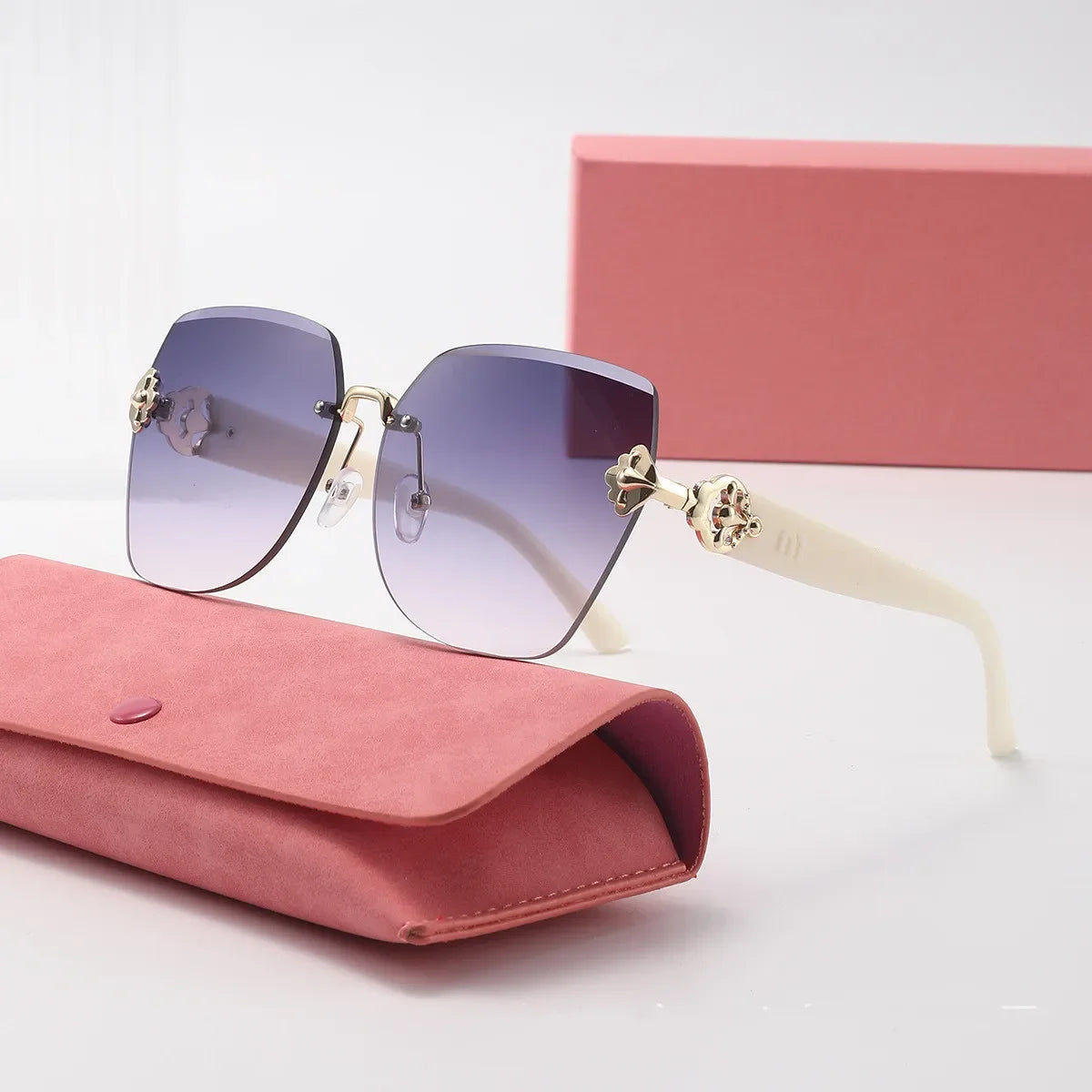 Sunglasses with gold accents and gradient lenses on a pink case with a matching box in the background.