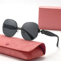 Black sunglasses with a floral design on the arm, placed on a pink case with a pink box in the background.