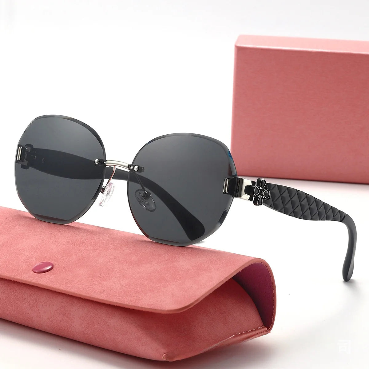 Black sunglasses with a floral design on the arm, placed on a pink case with a pink box in the background.