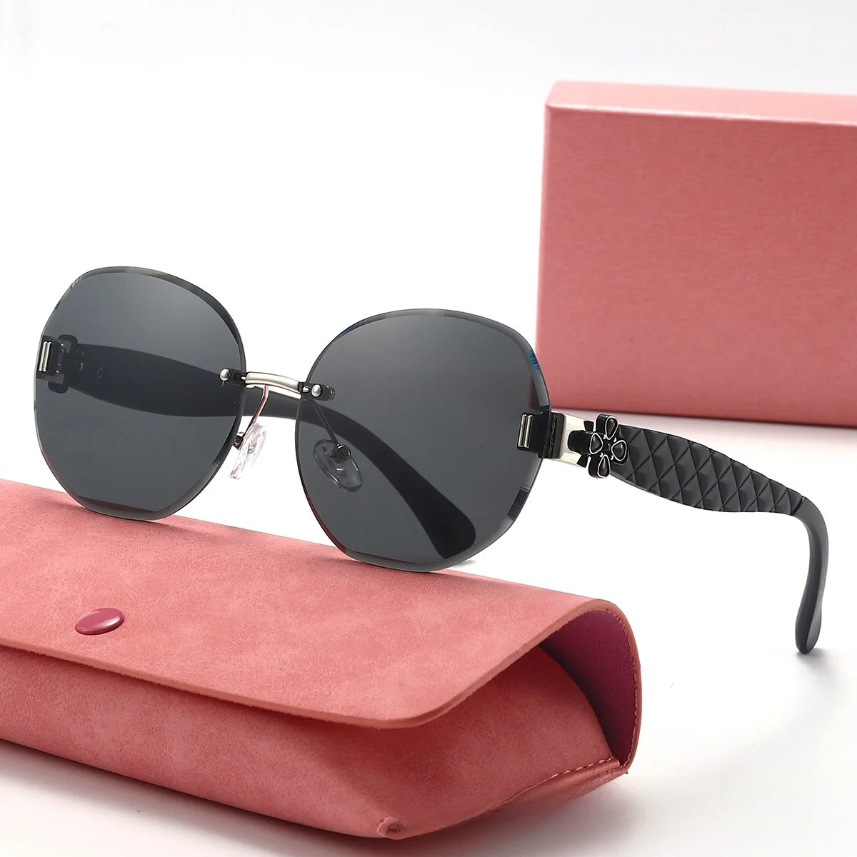 Black sunglasses with a floral design on the arm, placed on a pink case with a pink box in the background.