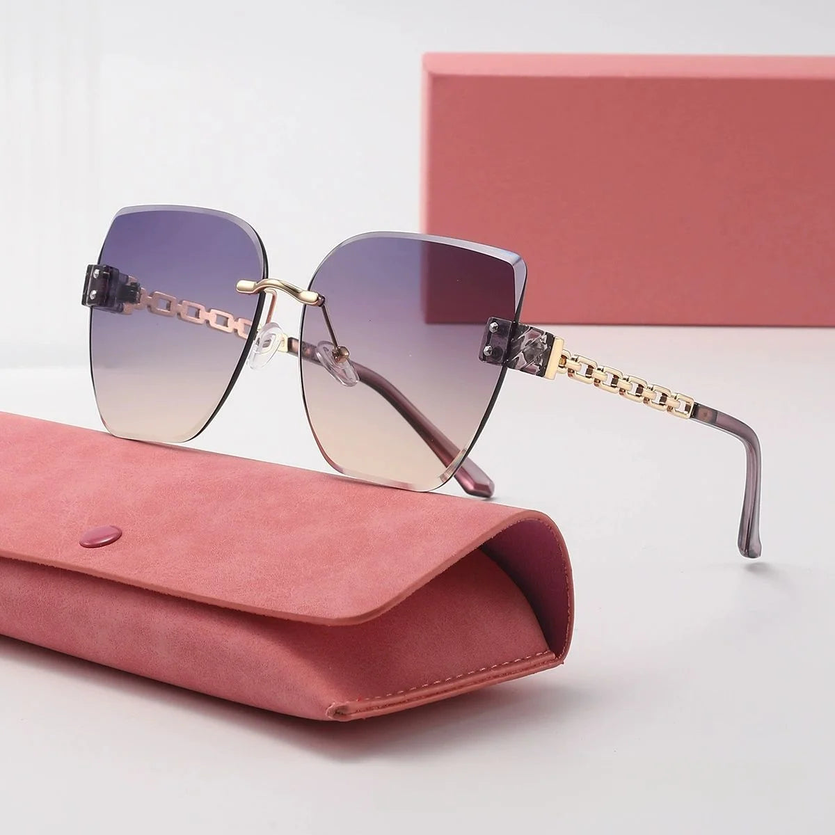 Sunglasses with gradient lenses and gold accents on a pink case with a matching box in the background.